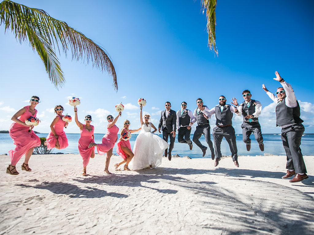 Bride, groom, and wedding party joyously leaping on the beach after their destination wedding ceremony in Florida.